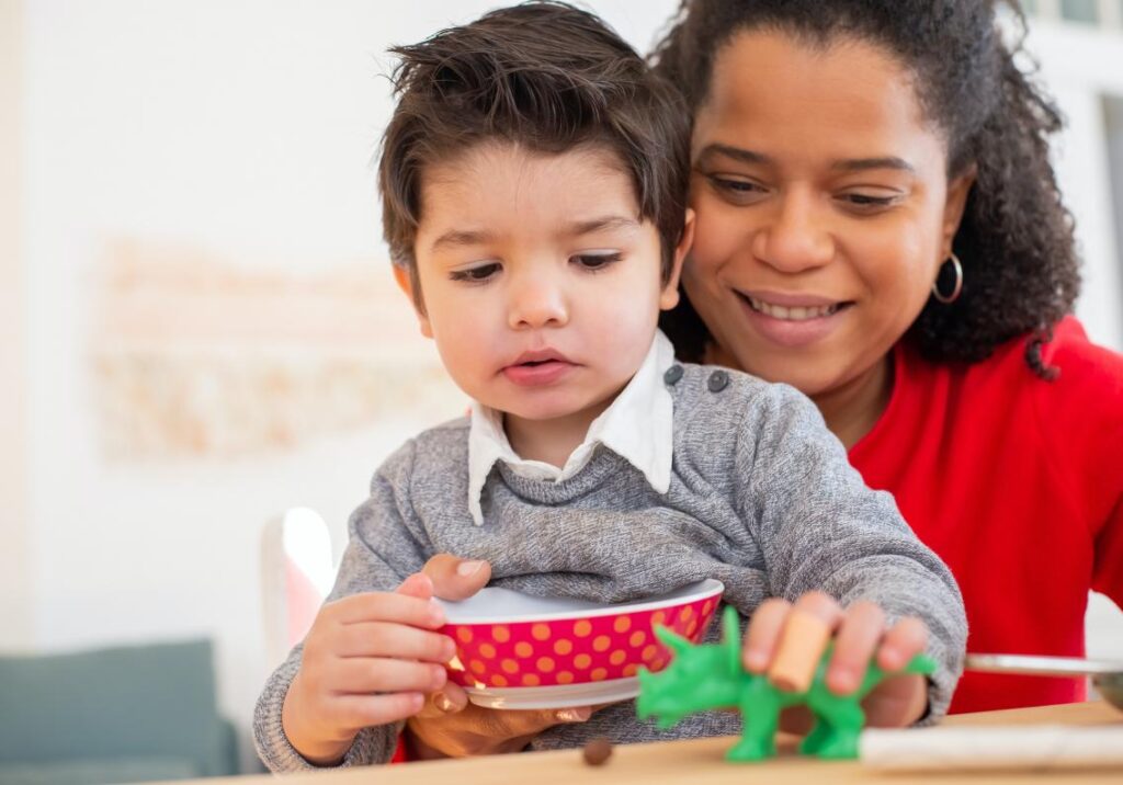 A young boy and woman play with a plastic green dinosaur.