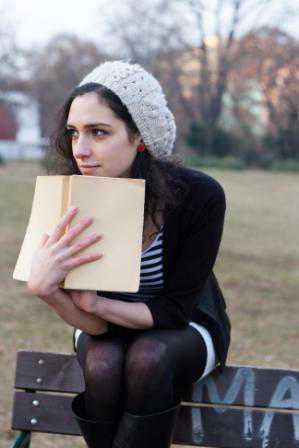 Teenage girl sitting on park bench holding a book